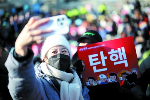 12月14日,在韩国首都首尔,一名在国会外参加要求弹劾总统尹锡悦集会的女子与一块写有“弹劾”字样的标语牌合影。新华社发